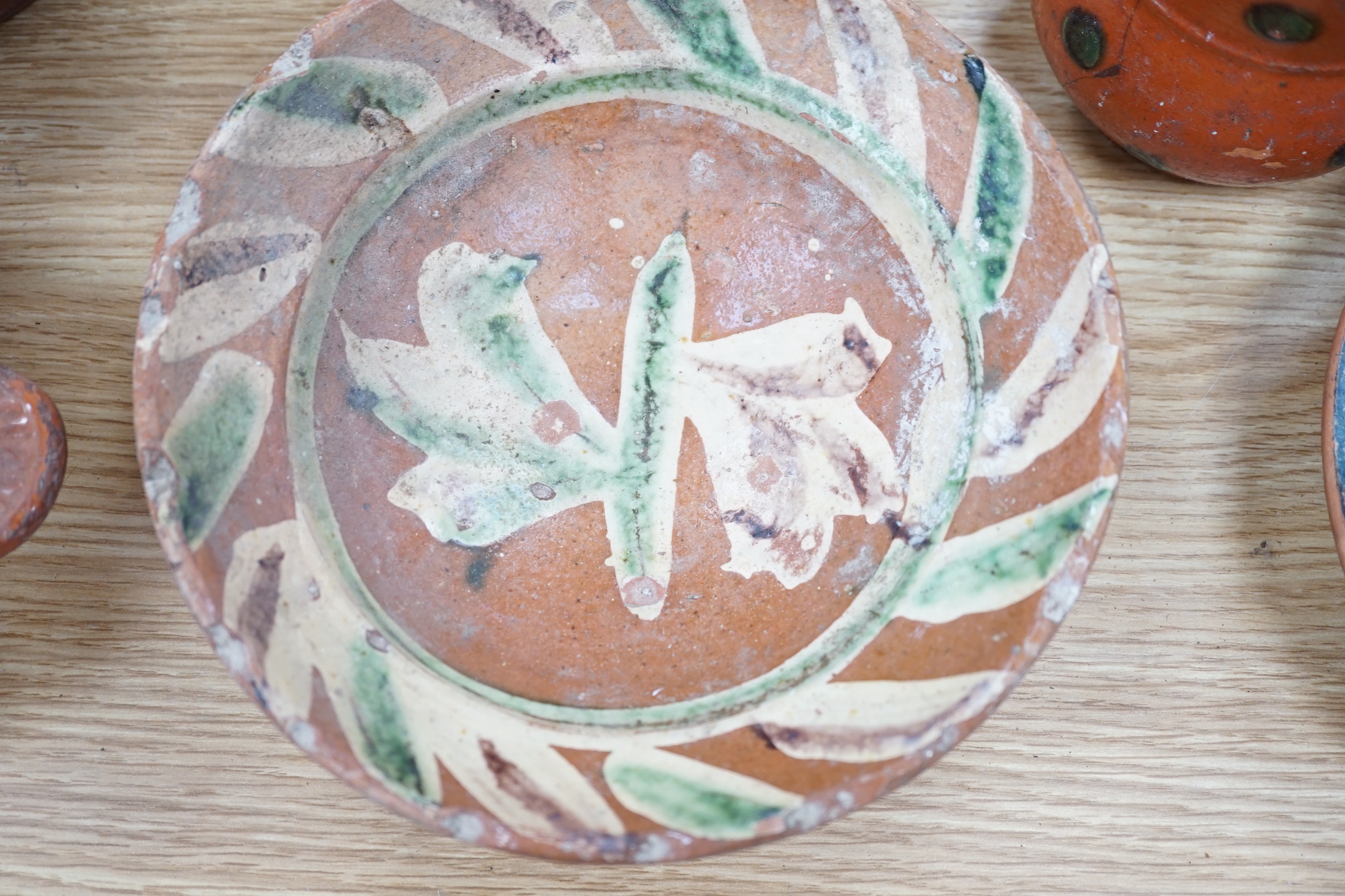 A group of Mediterranean slipware dishes, bowls and jugs, decorated in colours on a predominantly brown or ochre ground, the largest 33cm in diameter